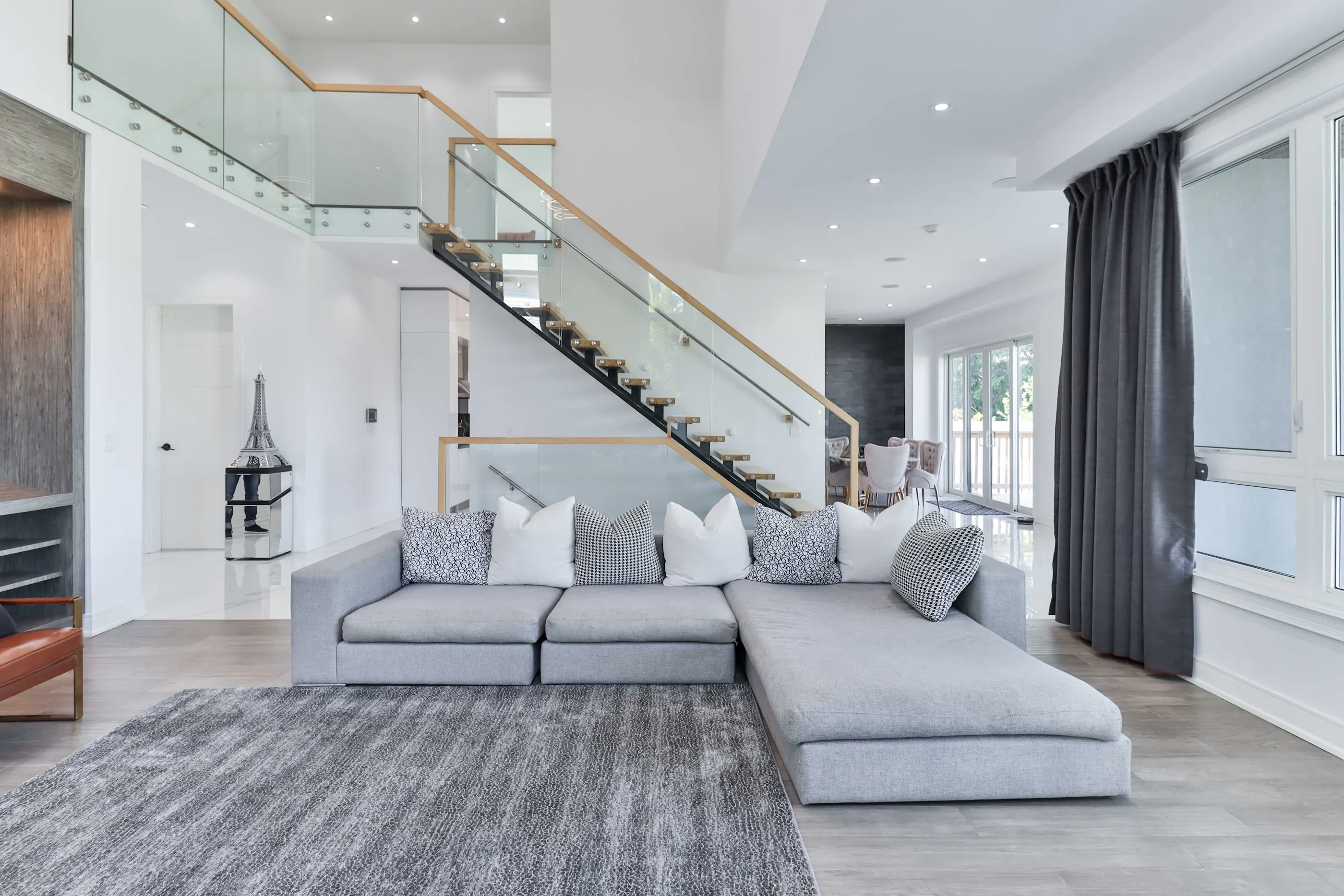 A spacious double-height living room with a glass staircase, neutral seating and large windows
